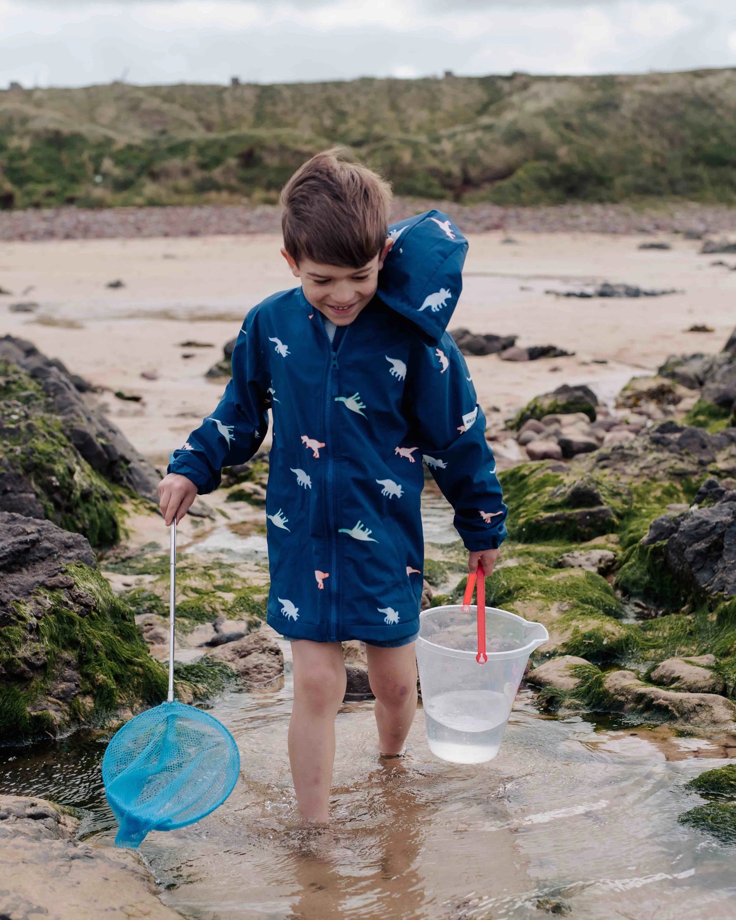 Holly and Beau boy on the beach wearing his dinosaur color changing raincoat